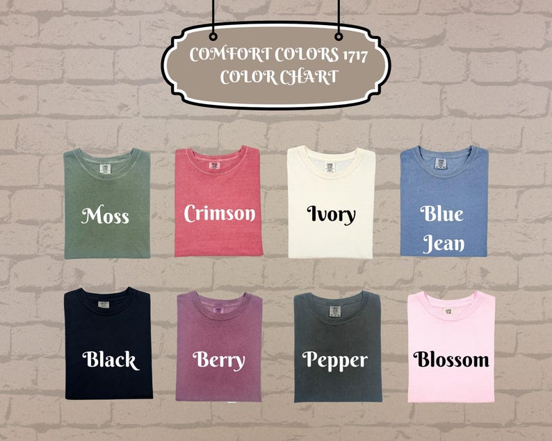 Pu&ograve; includere: Un campionario di colori mostra magliette piegate in vari colori, tra cui muschio, cremisi, avorio, blu jeans, nero, bacca, pepe e fioritura. Il testo "COMFORT COLORS 1717 COLOR CHART" &egrave; in alto. Le magliette sono su uno sfondo di muro di mattoni.