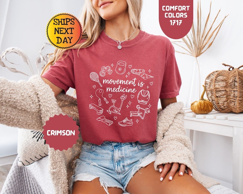 May include: Crimson-colored t-shirt with the text "movement is medicine" and fitness-related graphics in white. The shirt features a crew neck and short sleeves. The image also includes the words "Comfort Colors" and "Ships Next Day".