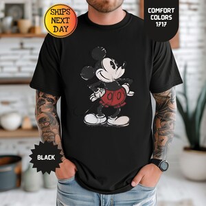 May include: Black t-shirt with a distressed Mickey Mouse graphic in black, white, and red. The shirt has the text "Comfort Colors 1717" and "Black". The cartoon character is in his classic pose.