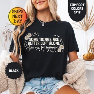 May include: Black t-shirt with the text "SOME THINGS ARE BETTER LEFT ALONE like me, for instance" in white. The shirt has a floral design and is labeled "BLACK" and "COMFORT COLORS 1717".