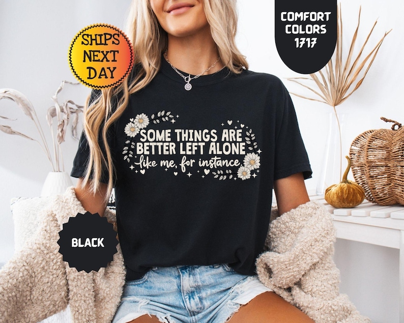 May include: Black t-shirt with the text "SOME THINGS ARE BETTER LEFT ALONE like me, for instance" in white. The shirt has a floral design and is labeled "BLACK" and "COMFORT COLORS 1717".