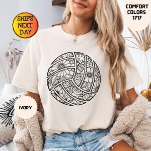May include: Ivory-colored t-shirt featuring a detailed black and white volleyball design. The volleyball is decorated with floral and geometric patterns. The shirt also has the text "Comfort Colors 1717" and "Ships Next Day".
