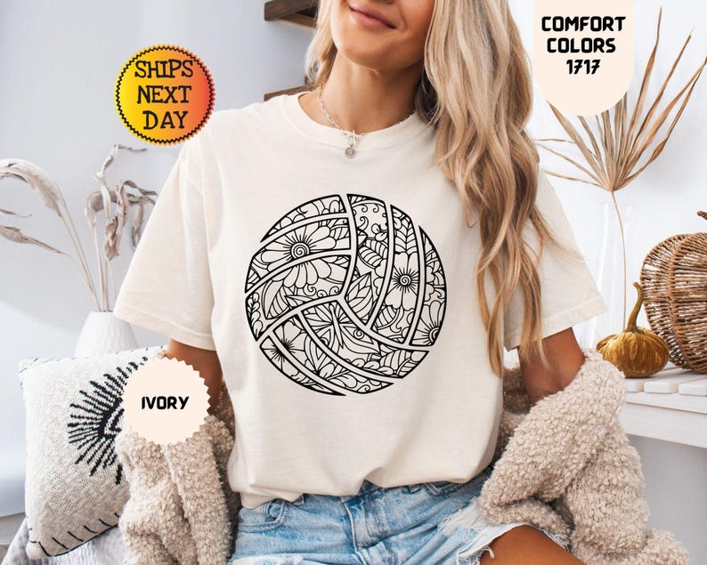 May include: Ivory-colored t-shirt featuring a detailed black and white volleyball design. The volleyball is decorated with floral and geometric patterns. The shirt also has the text "Comfort Colors 1717" and "Ships Next Day".