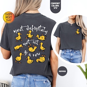May include: Dark gray t-shirt with the phrase "most definitely not all in a row" and cartoon ducklings. A small duckling graphic is on the front. The shirt is a Comfort Colors 1717, and the color is Pepper.