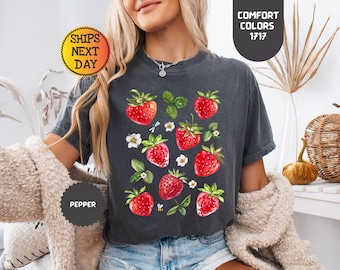 May include: A dark gray t-shirt with a graphic print of red strawberries and green leaves. The shirt has a relaxed fit and a crew neck.