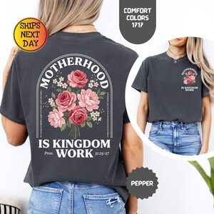Pu&ograve; includere: T-shirt grigio scuro con un design floreale e le parole "Motherhood Is Kingdom Work". Il design presenta rose rosa e rosse. La maglietta ha anche il testo "Prov. 31:25-27."