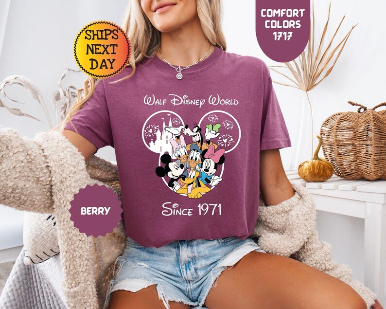 Pode incluir: Camiseta cor de berry com um design do Walt Disney World com Mickey Mouse e amigos. A camisa inclui o texto "Walt Disney World Since 1971". A camisa tem gola redonda e mangas curtas. A imagem tamb&eacute;m inclui o texto "Comfort Colors 1717".