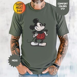 May include: A moss green t-shirt with a distressed Mickey Mouse graphic in black, white, and red. The shirt includes the text "Comfort Colors 1717" and "Ships Next Day".