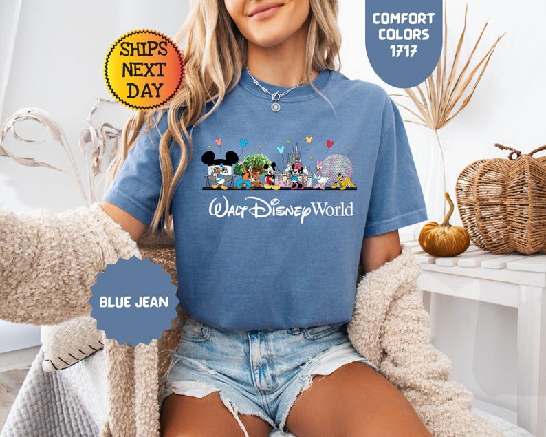 May include: Blue jean t-shirt featuring a Walt Disney World design with Mickey Mouse, Minnie Mouse, and other characters. The shirt has the text "Walt Disney World" in white. The shirt is a Comfort Colors 1717 style.