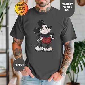 May include: Dark grey t-shirt with a distressed Mickey Mouse graphic. The cartoon character is in black, white, and red. The shirt has the text "Comfort Colors 1717" and "Ships Next Day".