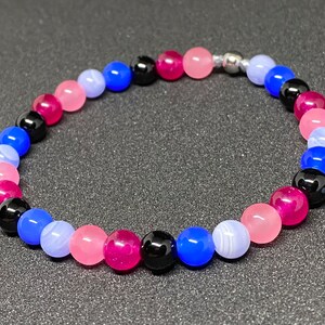 Könnte beinhalten: Ein mehrfarbiges Armband mit rosa, blauen und schwarzen Perlen. Das Armband besteht aus Edelsteinperlen und hat einen silbernen Verschluss.