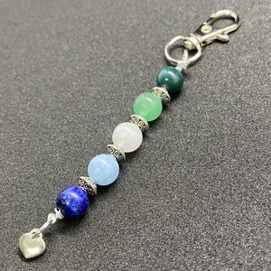 以下が含まれることがあります： ハートのチャームと青、緑、白のビーズのストランドが付いたシルバーのキーチェーン