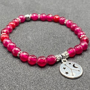 May include: A pink gemstone bracelet with a silver charm featuring a crescent moon and stars. The charm is attached to the bracelet with a silver clasp.