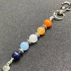 May include: A silver charm keychain with a heart charm and a series of colorful beads. The beads are blue, light blue, white, orange, and red.