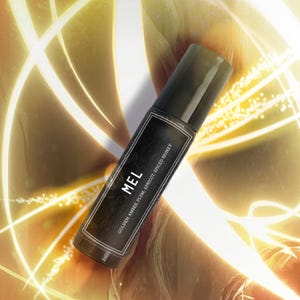 May include: A black roll-on perfume bottle with a label that reads "MEL" and "GOLDEN AMBER, PLUM, APRICOT, SPICED HONEY." The background features a golden, abstract design.