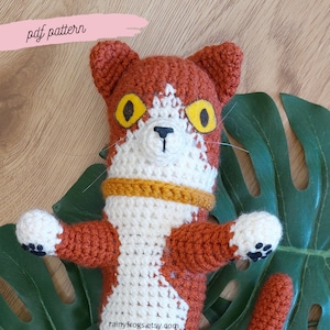 May include: Handmade crochet cat doll in orange, white, and yellow. The cat features large yellow eyes, a white face, and orange ears. The doll has a collar. The image includes the text "pdf pattern".