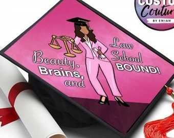 Puede incluir: Un birrete negro con una parte superior rosa que presenta una ilustración de dibujos animados de una persona con un traje rosa que sostiene una balanza de la justicia. El texto en la gorra dice "Beauty, Brains, and Law School Bound!". También hay un diploma enrollado con una cinta roja y una borla roja.