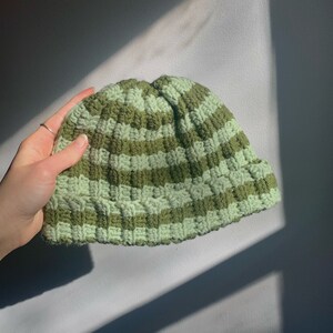 May include: A green and light green striped crocheted beanie hat.