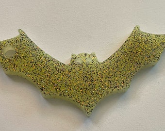 Pode incluir: Um ornamento verde com glitter em forma de morcego com um furo para pendurar.