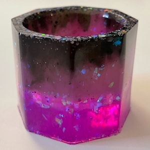 May include: A small, octagonal, clear resin container with a black and pink ombre effect. The container is filled with iridescent glitter.