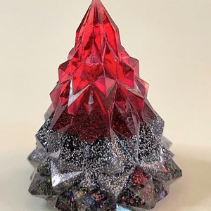 May include: A red and black resin Christmas tree ornament with a sparkly finish. The tree is shaped like a cone and has a pointed top.