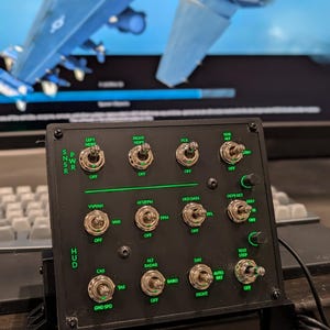 May include: A black control panel with multiple toggle switches and green text. The panel has labels like "LEFT HDPT," "RIGHT HDPT," and "HUD." The background shows a blurred image of a blue and gray aircraft.