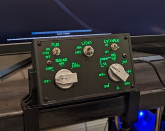 May include: A black panel with various switches and knobs, including a FLIR switch, LTD/R switch, LST/NFLR switch, and a RADAR knob. The panel has green and white text labels, including "FLIR", "LTD/R", "LST/NFLR", "RADAR", "INS", "NAV", "TEST", and "GYRO".