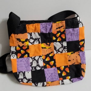 Può includere: Una borsa a tracolla a tema Halloween in patchwork nero e arancione con una tracolla nera. La borsa presenta fantasmi, pipistrelli, mais caramellato e ragnatele.