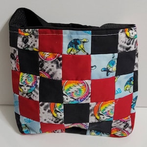 May include: A black, red, and blue patchwork tote bag with a checkered pattern. The bag features a tie-dye skull and crossbones design and a turtle design.