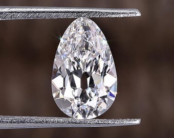May include: A pear-shaped diamond gemstone held in tweezers. The diamond is clear and has a brilliant cut.