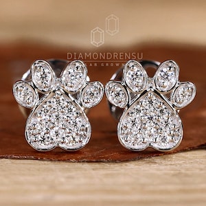 May include: A pair of silver paw print earrings with small diamonds set in the metal. The earrings are on a wooden surface.
