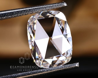 Könnte beinhalten: Ein klarer, kissenförmiger Diamant, der in einer Pinzette gehalten wird. Der Diamant hat eine brillante, facettierte Oberfläche.