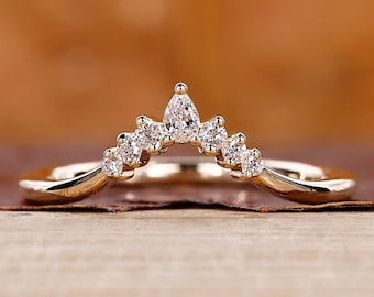 May include: A delicate gold ring with a curved band, set with small, sparkling diamonds. The diamonds are arranged in a graceful, upward-pointing arc, creating a crown-like design. The ring is displayed on a wooden surface.