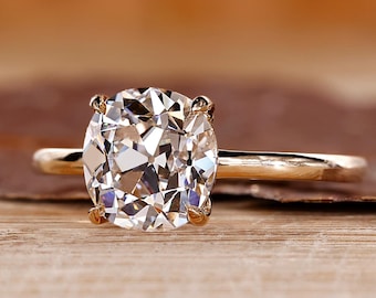 May include: A gold engagement ring with a large, clear, oval-cut diamond. The ring is set on a thin gold band. The diamond is the focal point, reflecting light and set against a blurred background.