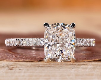 May include: A silver engagement ring with a large, cushion-cut diamond center stone and a pave diamond band.