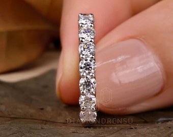 May include: A thin silver band with a row of small, round, clear diamonds set in a pave setting. The band is shown on a finger.