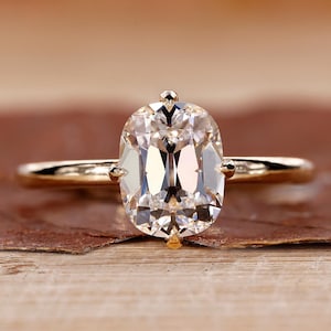 Może przedstawiać: Złoty pierścionek zaręczynowy z dużym, owalnym diamentem.