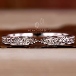 May include: A delicate, white gold wedding band with a curved, X-shaped design. The band is set with small, round diamonds.