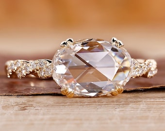 May include: A gold engagement ring with a large oval-shaped diamond and a twisted band accented with smaller diamonds.