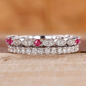May include: A set of two delicate silver rings with a row of small sparkling diamonds and a row of red gemstones.