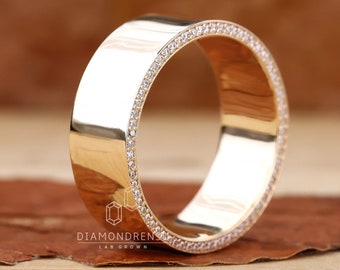 May include: A gold band with a row of small diamonds around the edge. The band is thick and has a polished finish. "DIAMONDRENS LAB GROWN" is printed on the band.