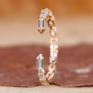 May include: A delicate gold ring with a row of small round diamonds and baguette diamonds. The ring is open on one side, making it adjustable.