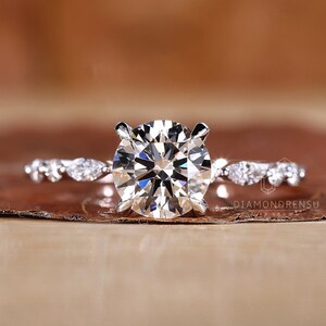 May include: A silver engagement ring with a large round diamond center stone and a delicate band of smaller diamonds. The ring is set on a brown background.
