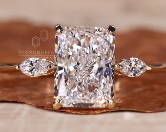 May include: A gold engagement ring with a large, rectangular, clear diamond center stone and two smaller, pear-shaped diamonds on either side.