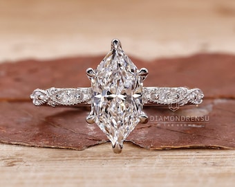 Op de afbeelding: Een verlovingsring met een marquise-geslepen diamant en een delicate, vintage-geïnspireerde band. De ring heeft een sprankelende, heldere diamant die in een grijpbevestiging is gezet. De band is versierd met kleinere diamanten en ingewikkelde details.