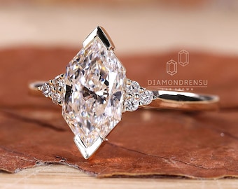 May include: A gold engagement ring with a large, clear, marquise-shaped diamond. The diamond is set in a prong setting and has a pointed tip. The ring also has smaller diamonds set on either side of the main diamond.