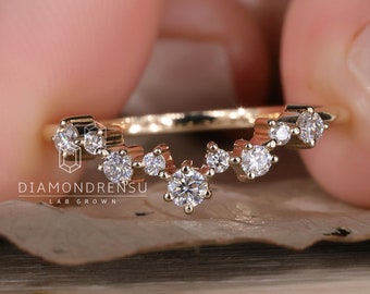 Può includere: Un delicato anello d'oro con un design curvo adornato con una fila di piccoli diamanti. L'anello è posto su una superficie testurizzata.
