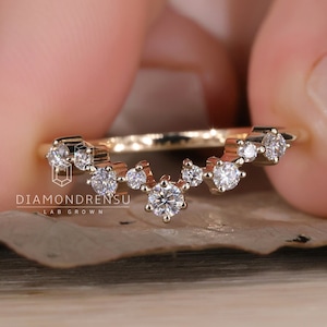Op de afbeelding: Een delicate gouden ring met een gebogen ontwerp met een rij kleine diamanten. De ring ligt op een getextureerd oppervlak.