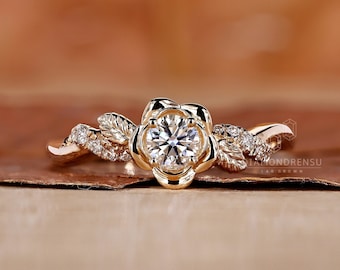 May include: A gold ring with a diamond set in a flower-shaped setting. The ring is adorned with delicate leaves and small diamonds.