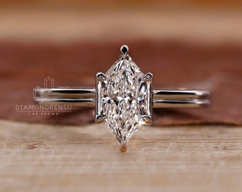 May include: A silver ring with a large, clear, marquise-shaped diamond. The ring has a simple band and is set on a wooden surface.